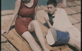 Two bathers in bathing suits sitting on a deck.