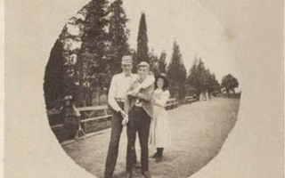 A group of three stand closely together in front of a fence and trees.