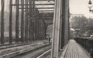 Closeup of a bridge and train tracks. A man appears in the distance.