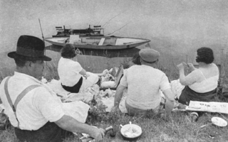 A group of men and women sitting together on a river bank. They watch a boat passing by.