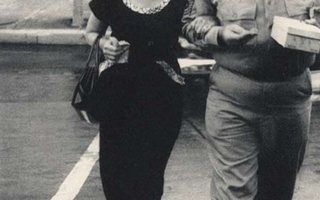 A woman wearing a black dress walks with a man in uniform.