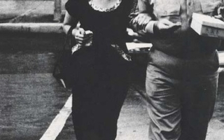 A woman wearing a black dress walks together with a man in uniform.